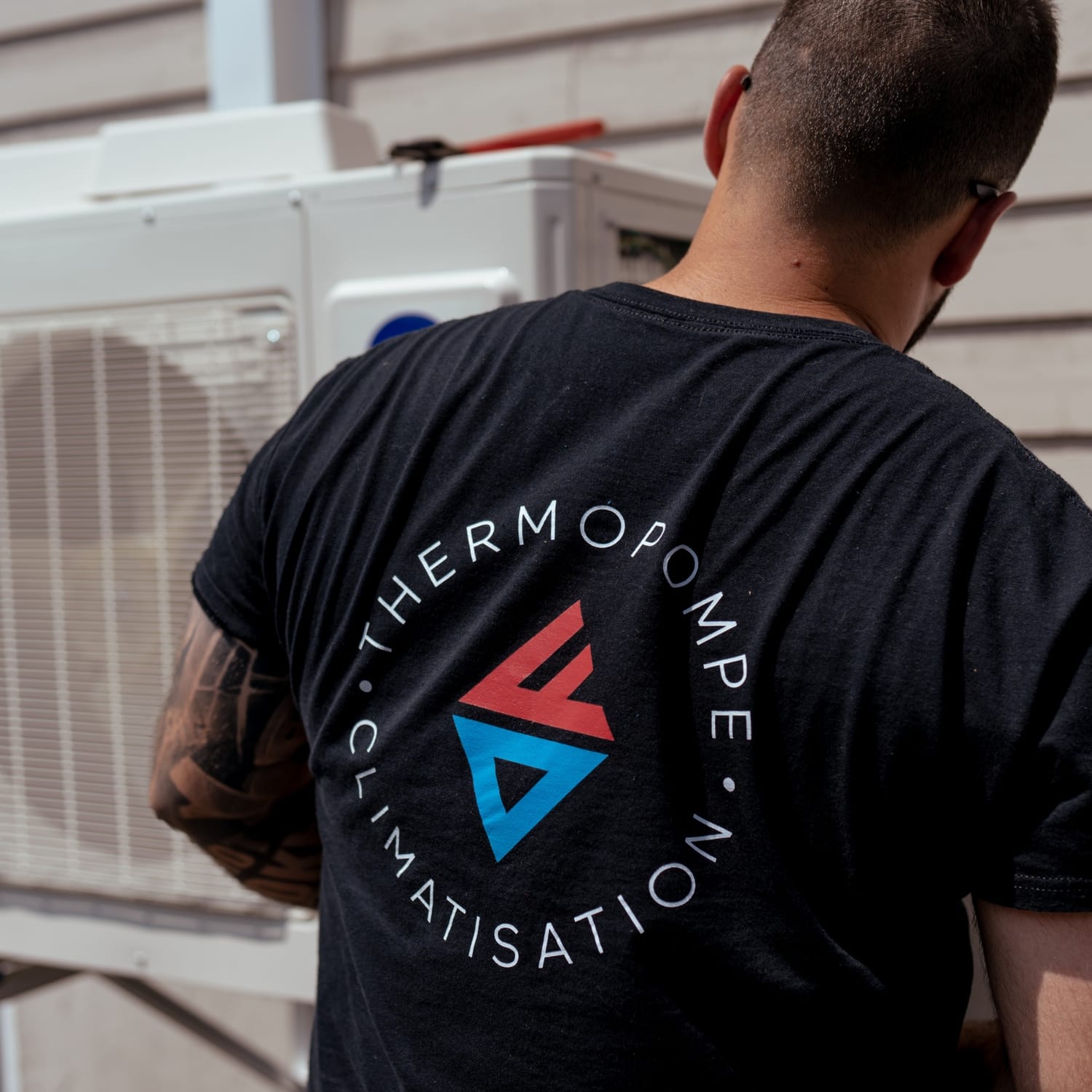 Technicien TCDF de dos devant une thermopompe